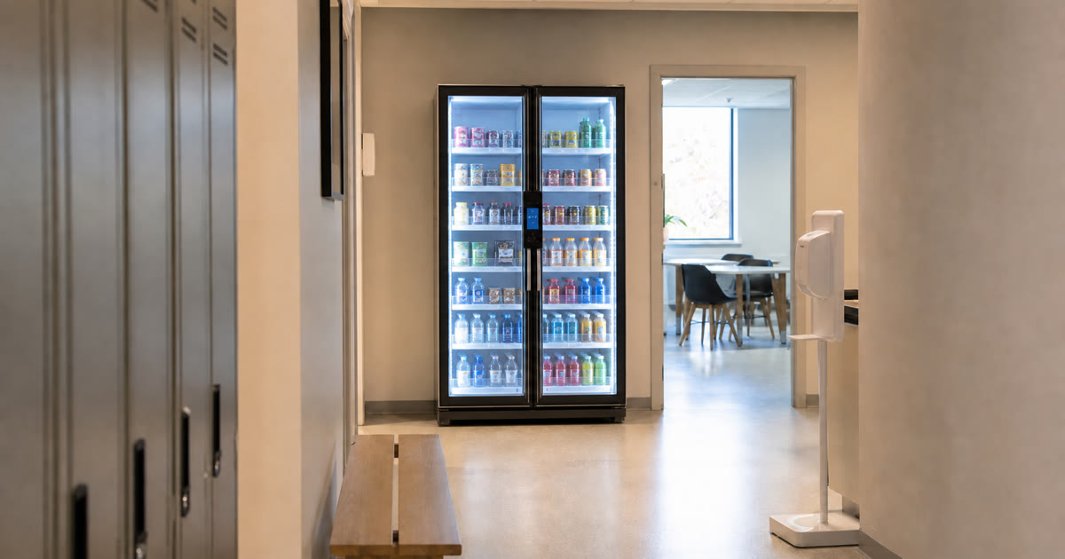 Conceptual Revvolto smart vending cooler in a staff-only Austin medical office corridor near lockers